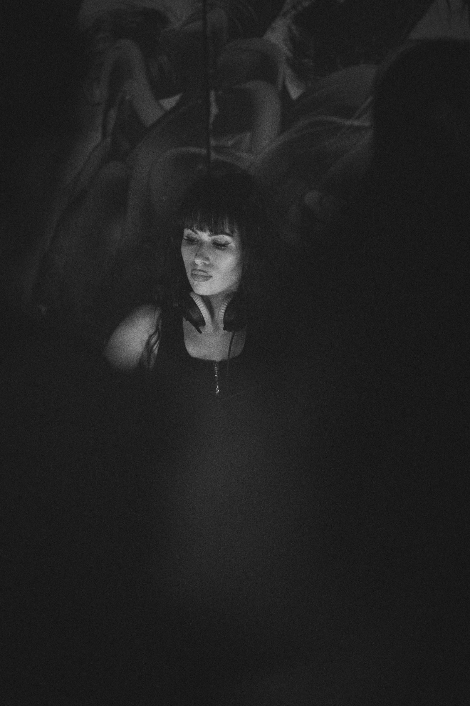 A DJ between sets, headphones around the neck, under a low ceiling of crowd silhouettes