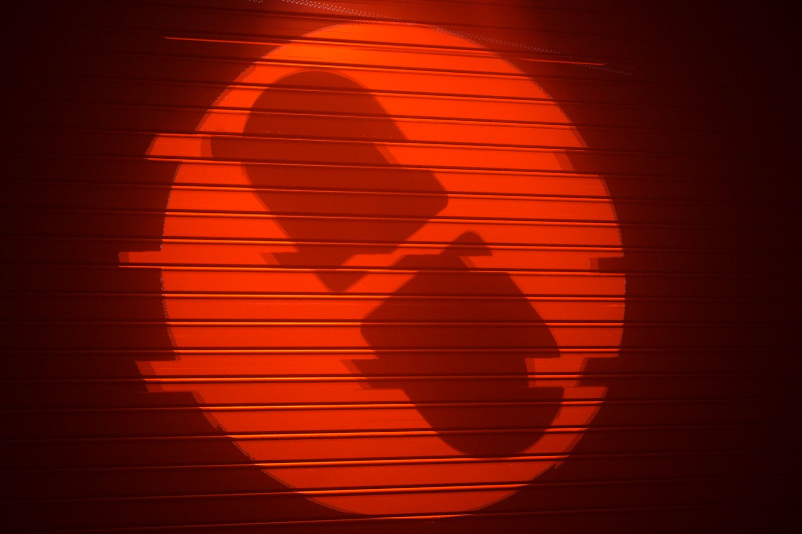 Two silhouettes against a red circle of light on a slatted warehouse wall