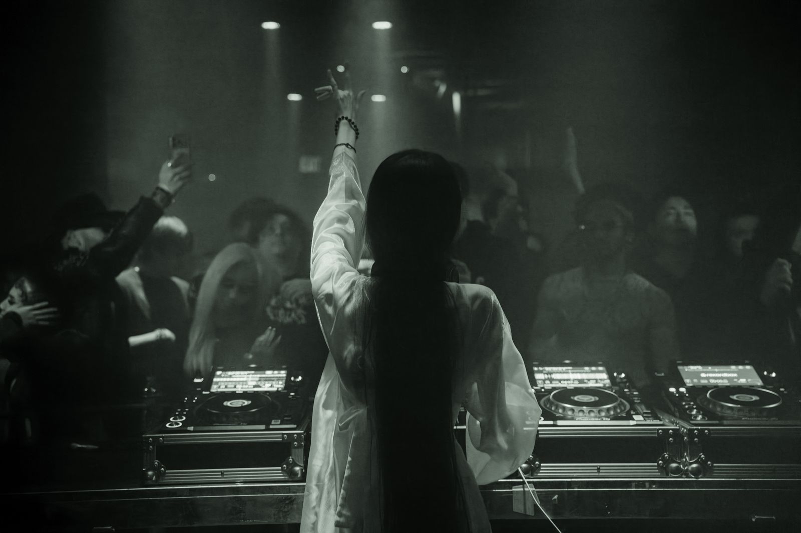 Pisapia behind the decks, arm raised to the room. The Woodshop holds the moment in monochrome.