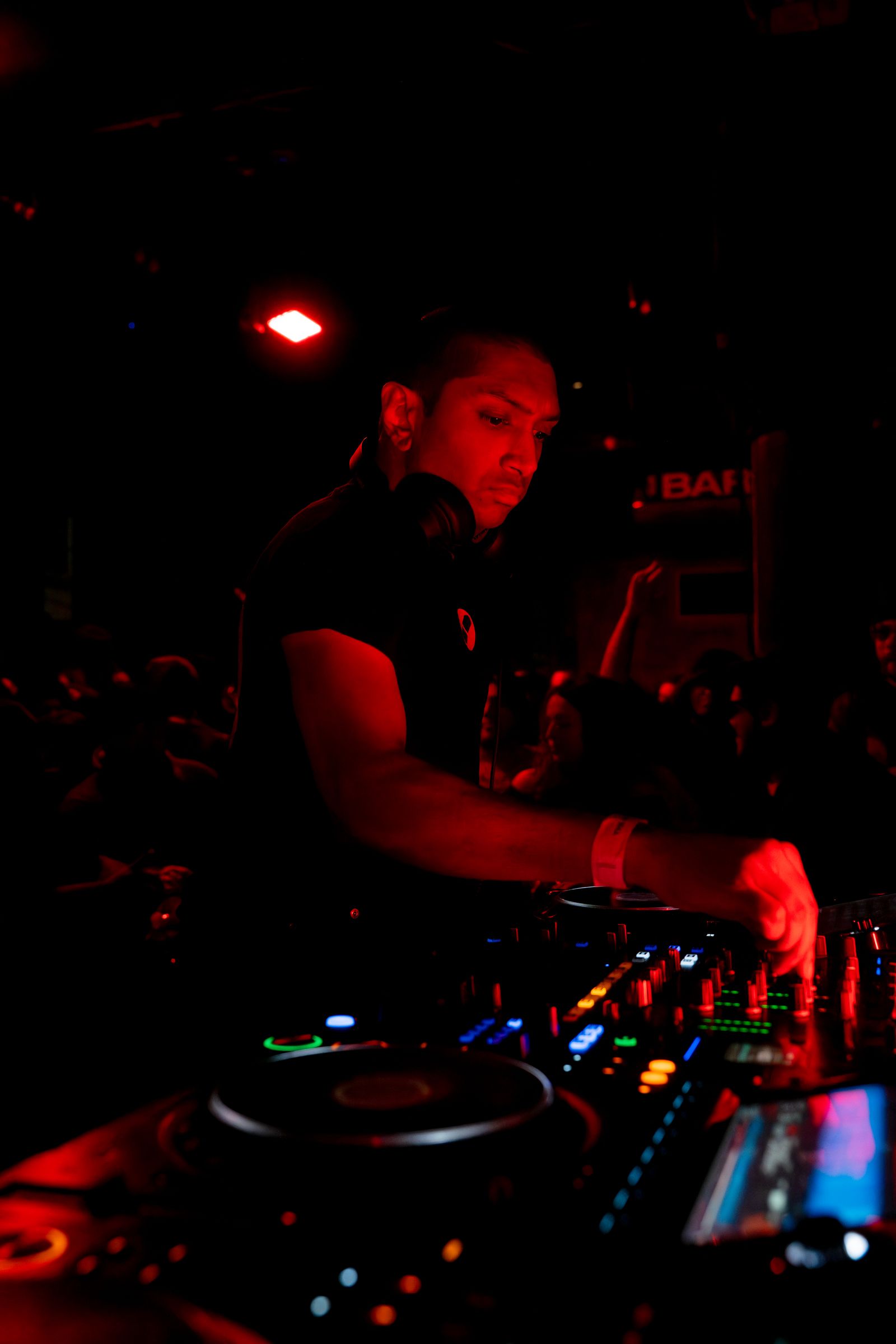 A DJ at the decks under a single red light, the crowd fading into the dark behind